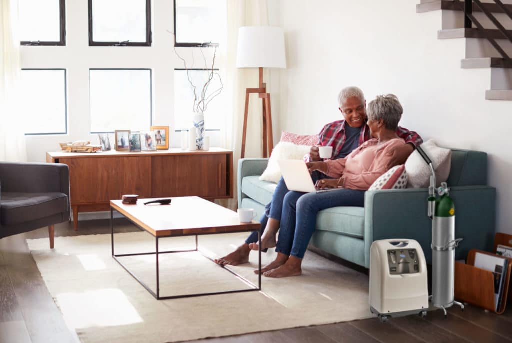 Couple sits in living room next to portable oxygen concentrator