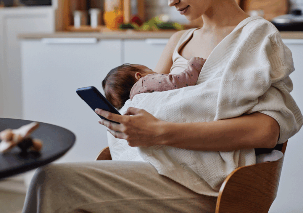 Mother holding newborn while researching best breast pumps on her phone