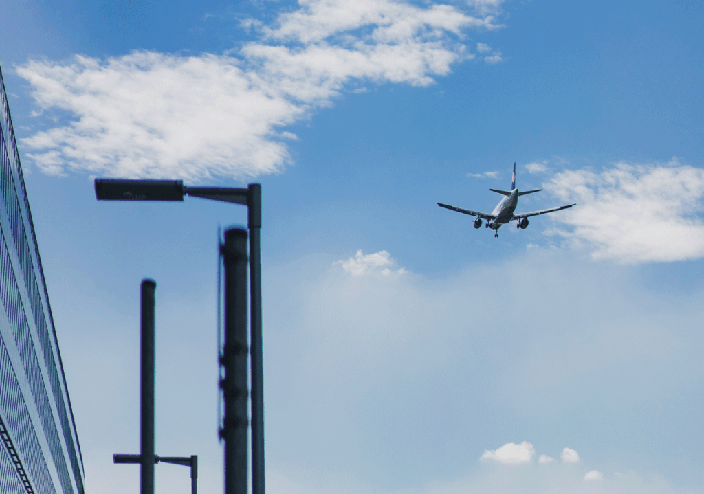 Airplane flying in a clear blue sky near buildings, symbolizing air travel.