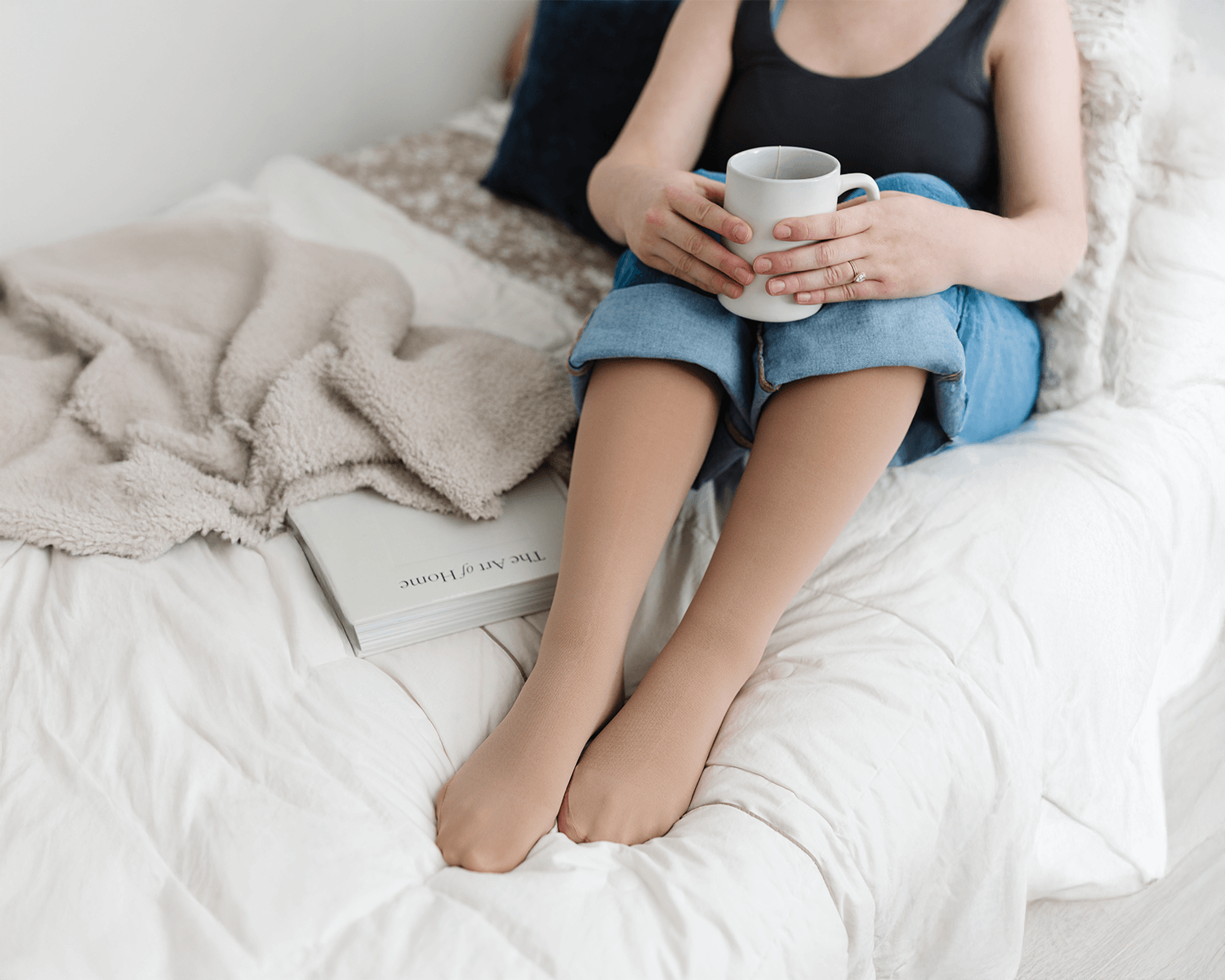 A woman wearing compression stockings sitting in bed with a mug